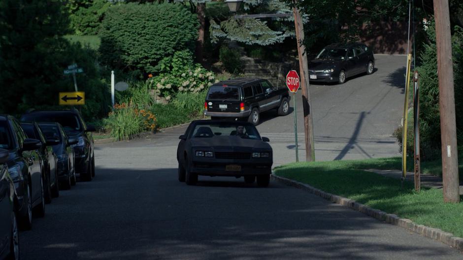 Erik drives his car down the street in front of the house.