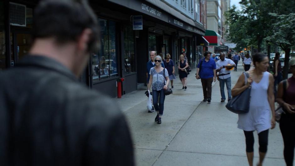 Erik walks past people on the street trying to control his headache.