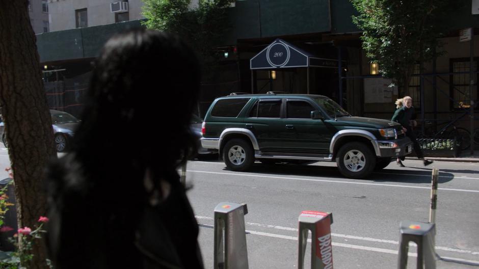 Jessica watches as Trish runs across the street after jumping down from the building.