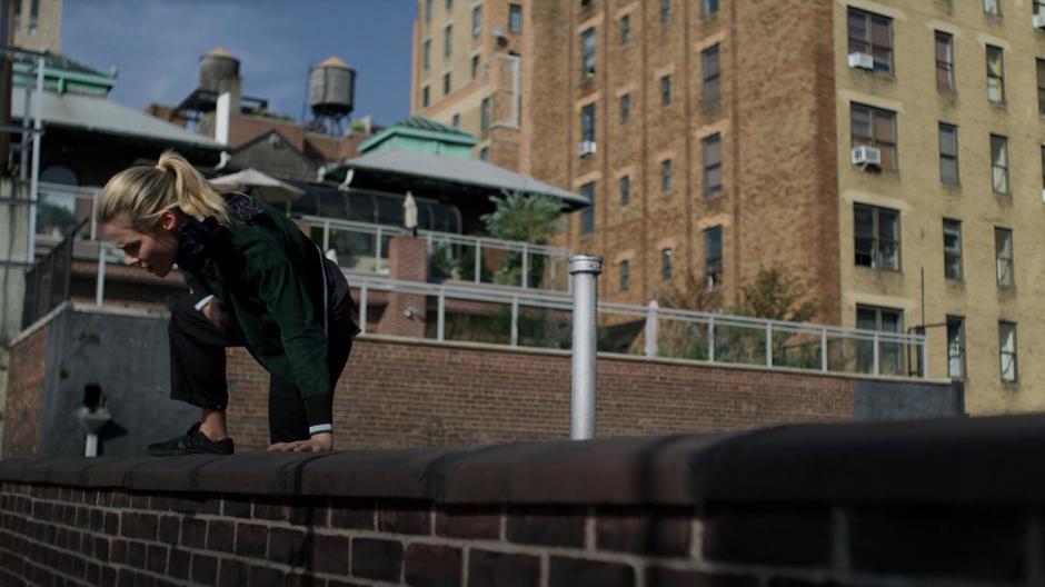 Trish climbs on the edge of the roof and checks how far the drop is.