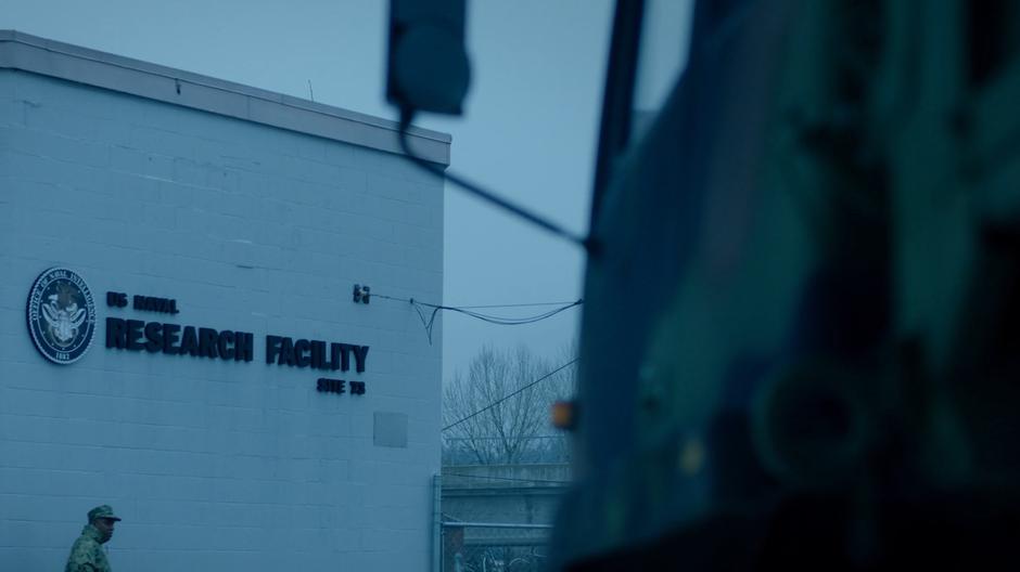 Exterior shot of the lab while a soldier walks past on patrol.