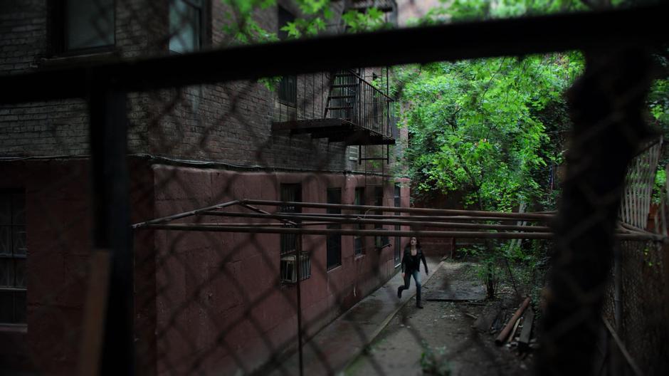 Jessica walks around the back of the building looking up at the fire escape.