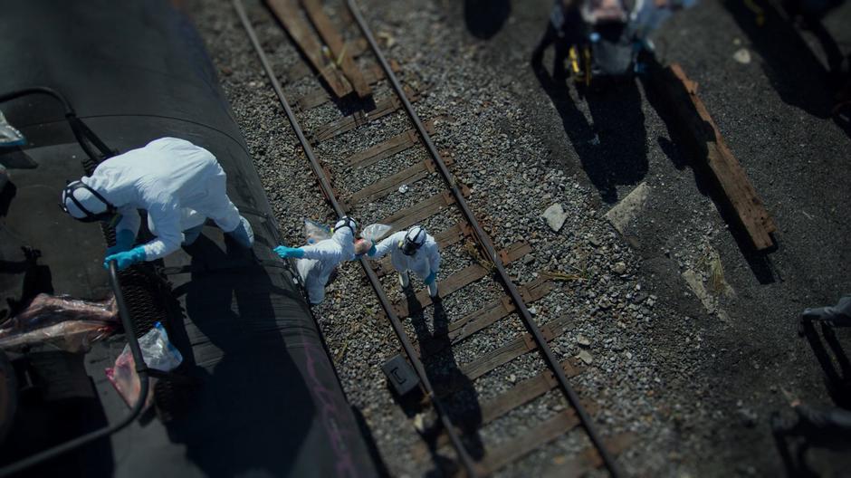 Workers in hazmat suits pass down body parts from the tanker car.