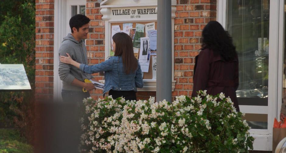 Stephanie puts her hand on Sean's shoulder as they are both putting up fliers.