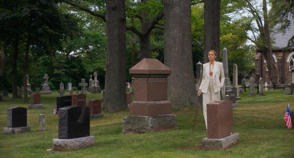 Emily strolls through the graveyard wearing a white suit.