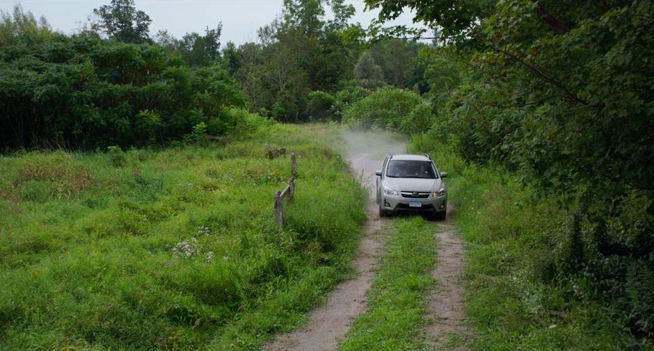 Stephanie drives down a dirt driveway through the woods.