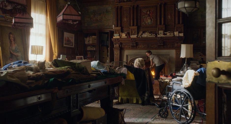 Stephanie leans down in front of the fire while talking to Margaret McLanden.