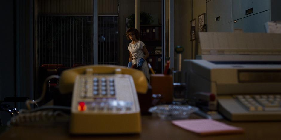 Nancy looks up at the ringing phone from where she is cleaning up the office.