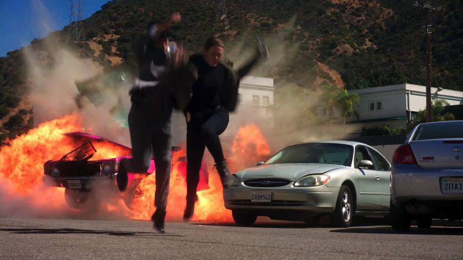 Lucifer and Chloe dive through the air as the car explodes behind them.