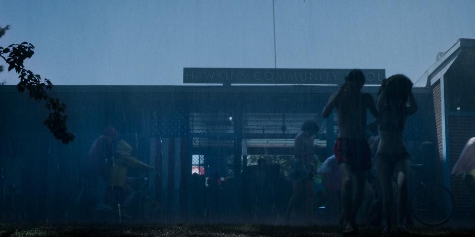 Eleven and Max ride up to the front of the pool on Max's bike as people run out through the pouring rain.