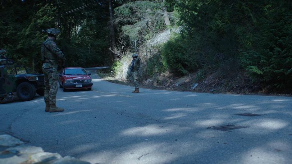 Helen drives between two soldiers standing in the road.