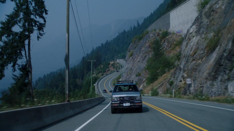 Maddie and Ben drive down a road beside a steep cliff.