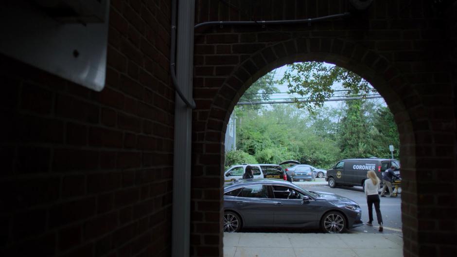 Trish walks around her car to Jessica who is on the phone while the coroner loads up the body.