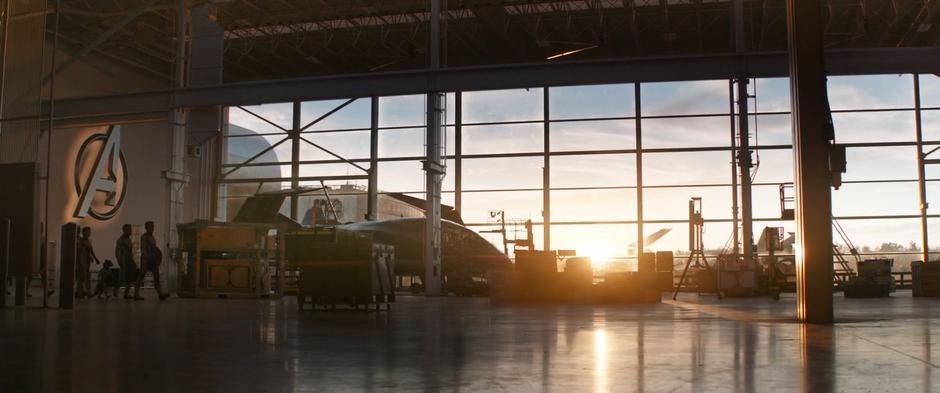 The remaining Avengers walk across the warehouse floor at sunset to the time machine.