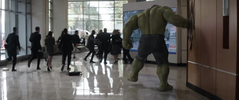 The Hulk punches a wall in the lobby after smashing out of the stairwell.