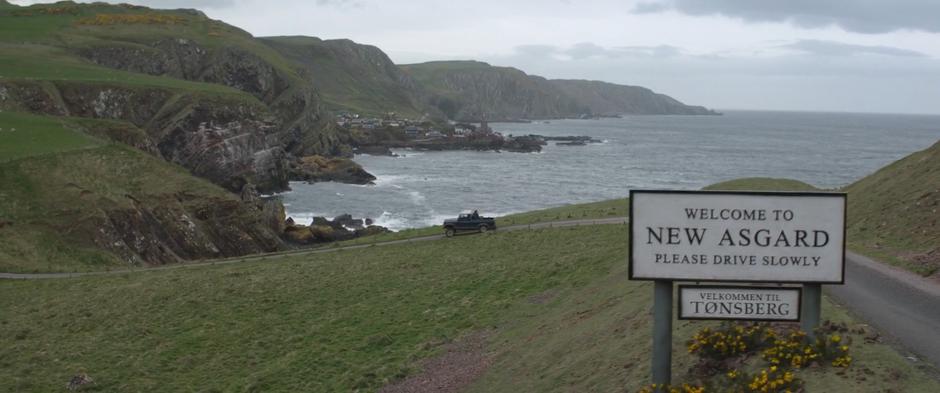 The truck turns the corner past the "Welcome to New Asgard" sign.