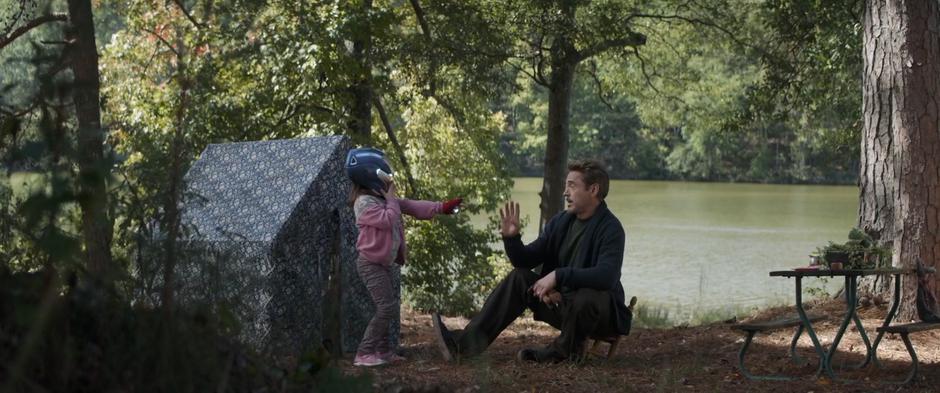 Tony sits on a tiny chair and plays with his daughter Morgan who is dressed in an Iron Man helmet and glove.