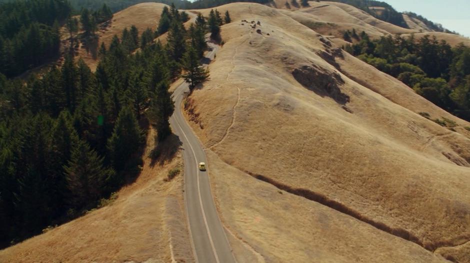 Bumblebee drives down the winding hilltop road toward some trees.