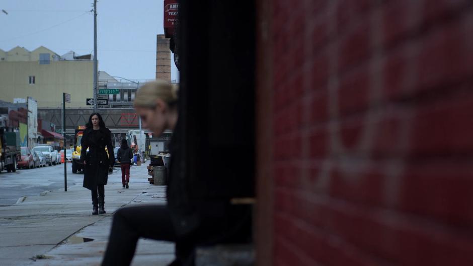 Jessica walks down the sidewalk to where Trish is sitting on her front steps.