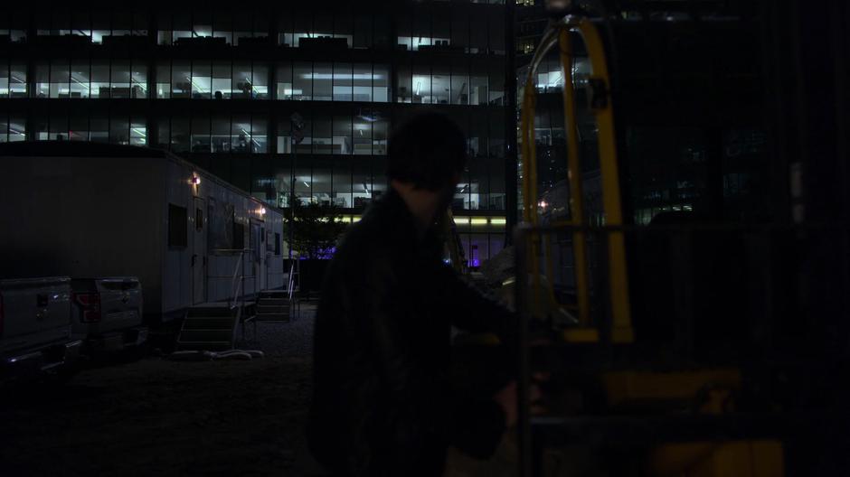 Erik looks over at the construction trailer while he stands near a piece of equipment.