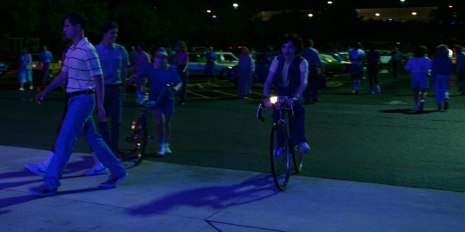 Mike rides up onto the sidewalk towards the bike rack.