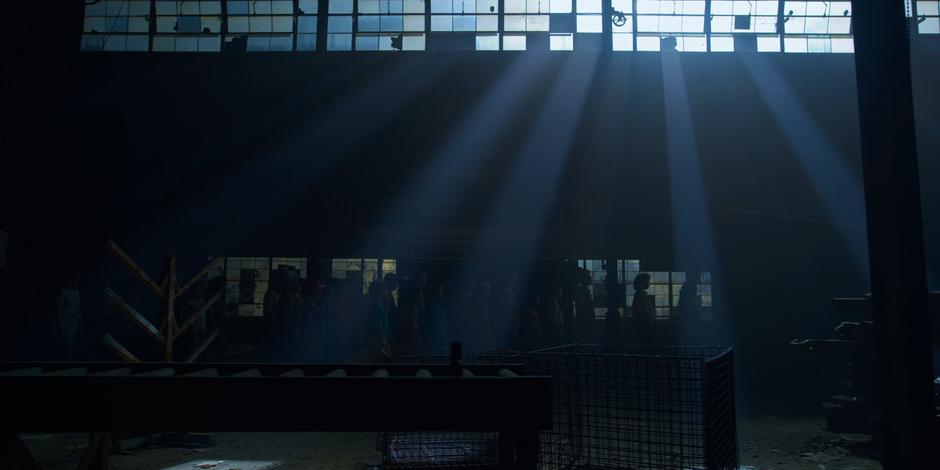 A line of controlled people walk through the building towards the basement.