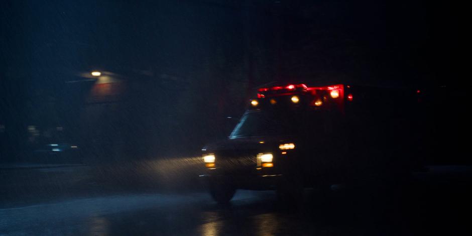 The ambulance carring Mrs. Driscoll drives past the abandoned building.