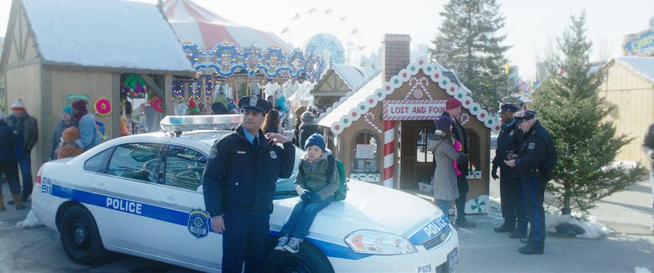 Young Billy sits on the hood of a police car while the officer calls in his missing mother.