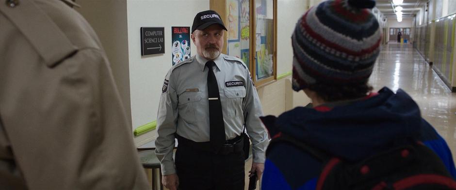 The security guard looks skeptically at Billy in his superhero form who is telling him to let Freddy leave for the day.