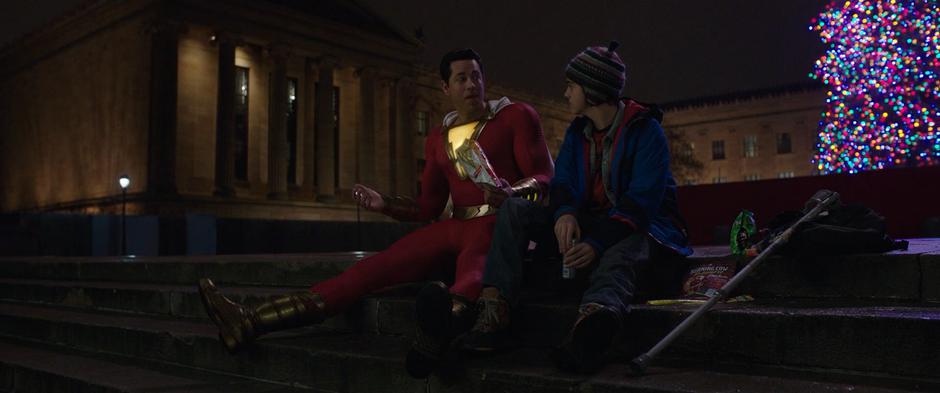 Billy and Freddy sit on the steps of the museum talking and eating junk food.