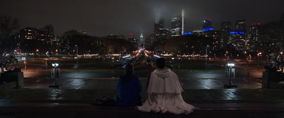 Freddy and Billy sit on the steps looking out over the city at night.