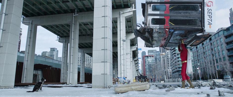 Billy holds the bus above his head while urging the dog to move out of the way so he can put it down.