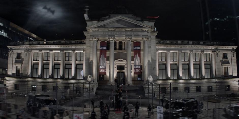 The crowd works its way through security at the steps of the museum as the Bat-Signal shines in the sky.