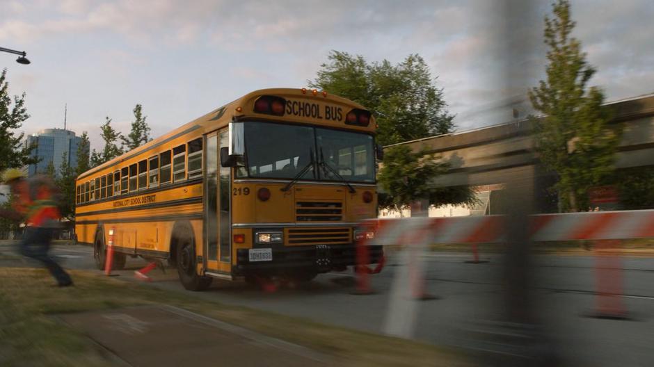 The runaway school bus crashes through some construction barriers.