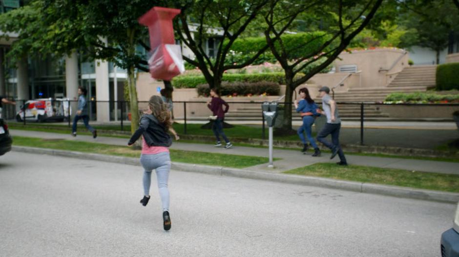 People run down the street as a newspaper box is thrown overhead.