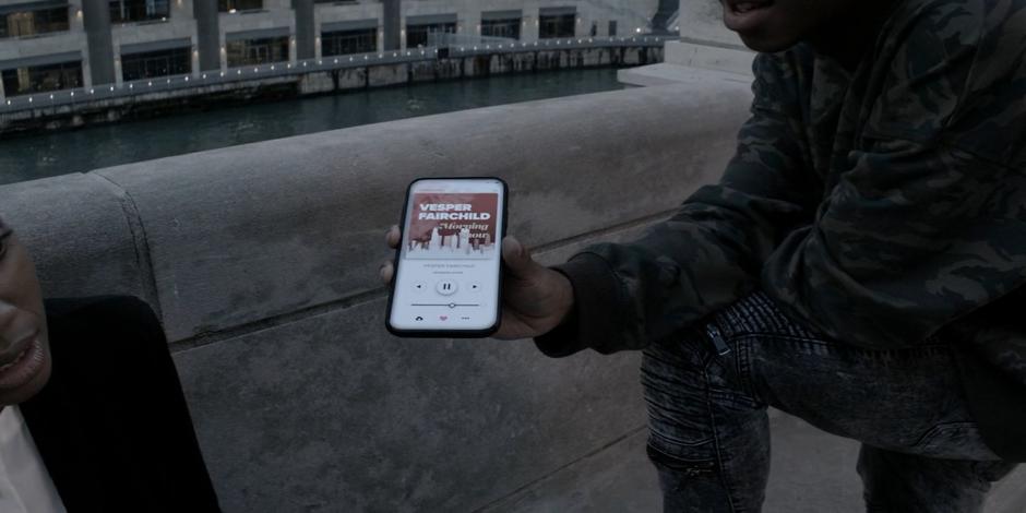 A kid holds his phone up with the Vesper Fairchild Morning Show playing for his friends while he stands with one foot on a bench.