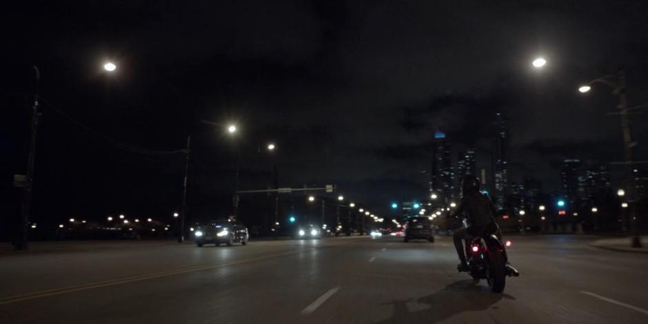 Kate rides her motorcycle through an intersection at night.
