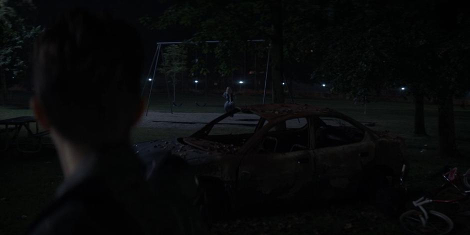 Kate looks over and sees Alice on a nearby swingset past at abandoned car.