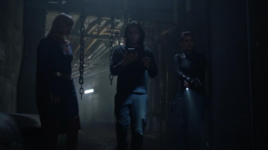 Kara and Alex keep an eye out while Brainy follows the signal on his device.