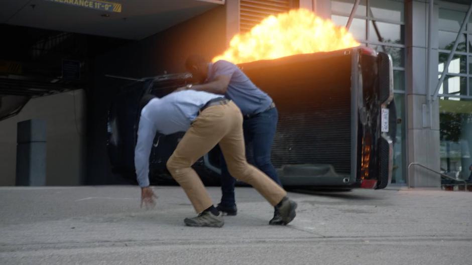 J'onn pulls a bystander out of danger as a truck explodes behind them.