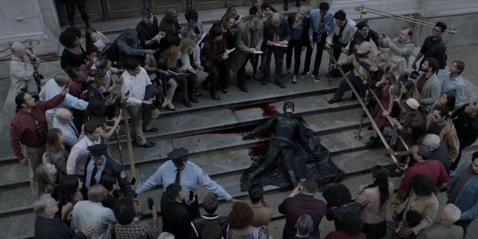 Police officers hold off the crown looking at the dummy dressed as Batman and surrounded by blood on the steps.