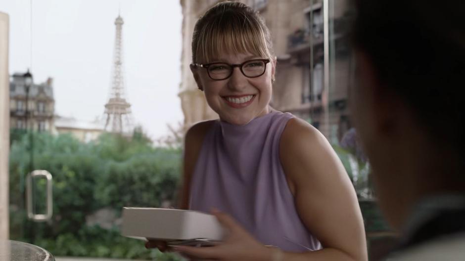 Kara smiles at the cashier while holding the snacks she bought for Lena.
