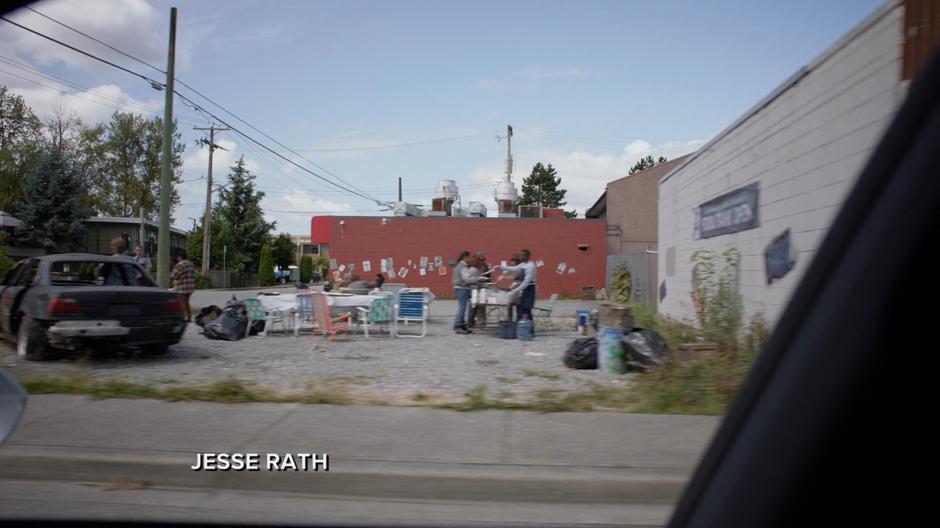 A line of people get food from a table set up in the middle of an empty lot.