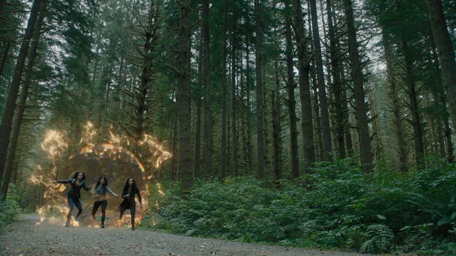 Abigael, Mel, and Macy hope out of the portal onto a dirt road through the woods.