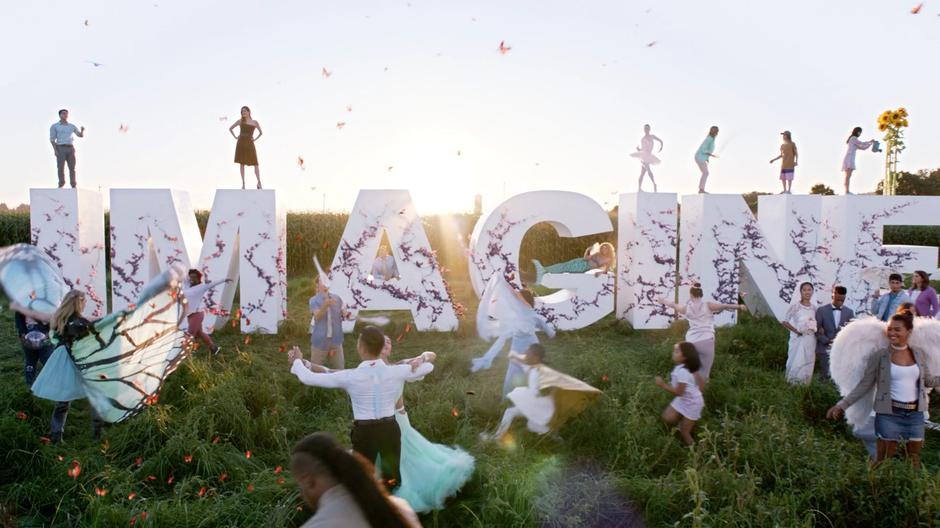 Andrea stands on top of a giant Imagine sign while people dance around and on top of it during the announcement video.