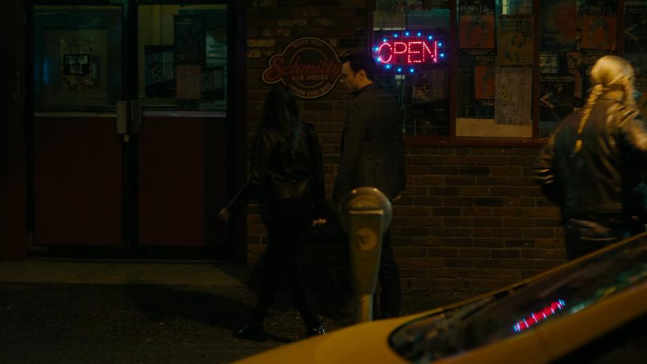 Mel and Harry look up at the sign as they walk to the door of the bar.