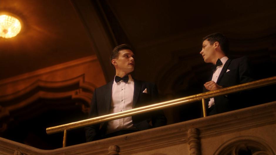 Ralph and Barry stand on the balcony above the lobby as Ralph tells Barry about all of the underworld players at the auction.