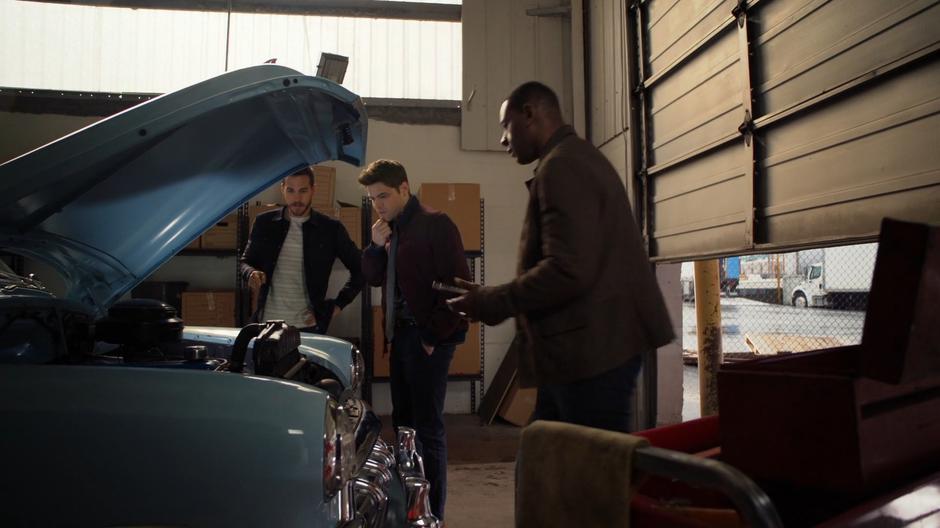 Winn and J'onn look down at the engine of the spaceshipcar.