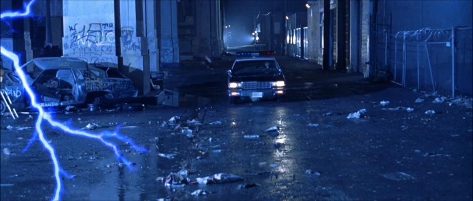 A police officer drives his car to the end of the street where lightning is striking.