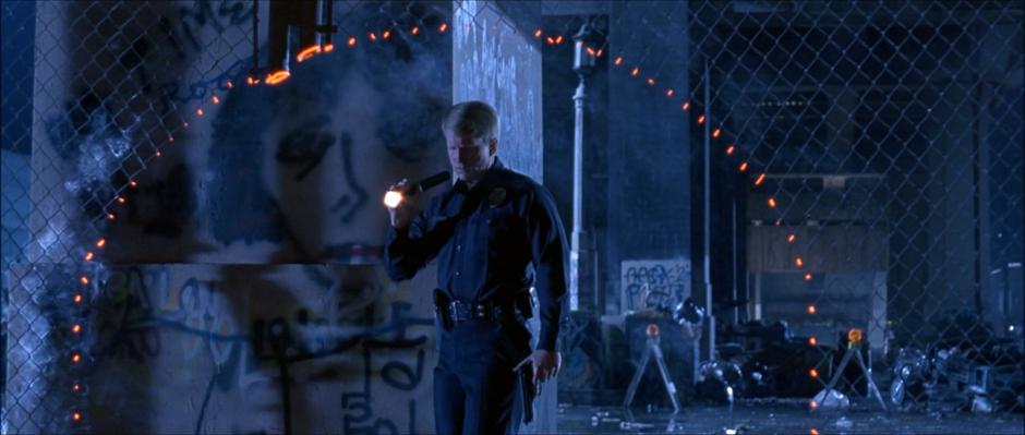 A police officer investigates a circular hole in the fence.